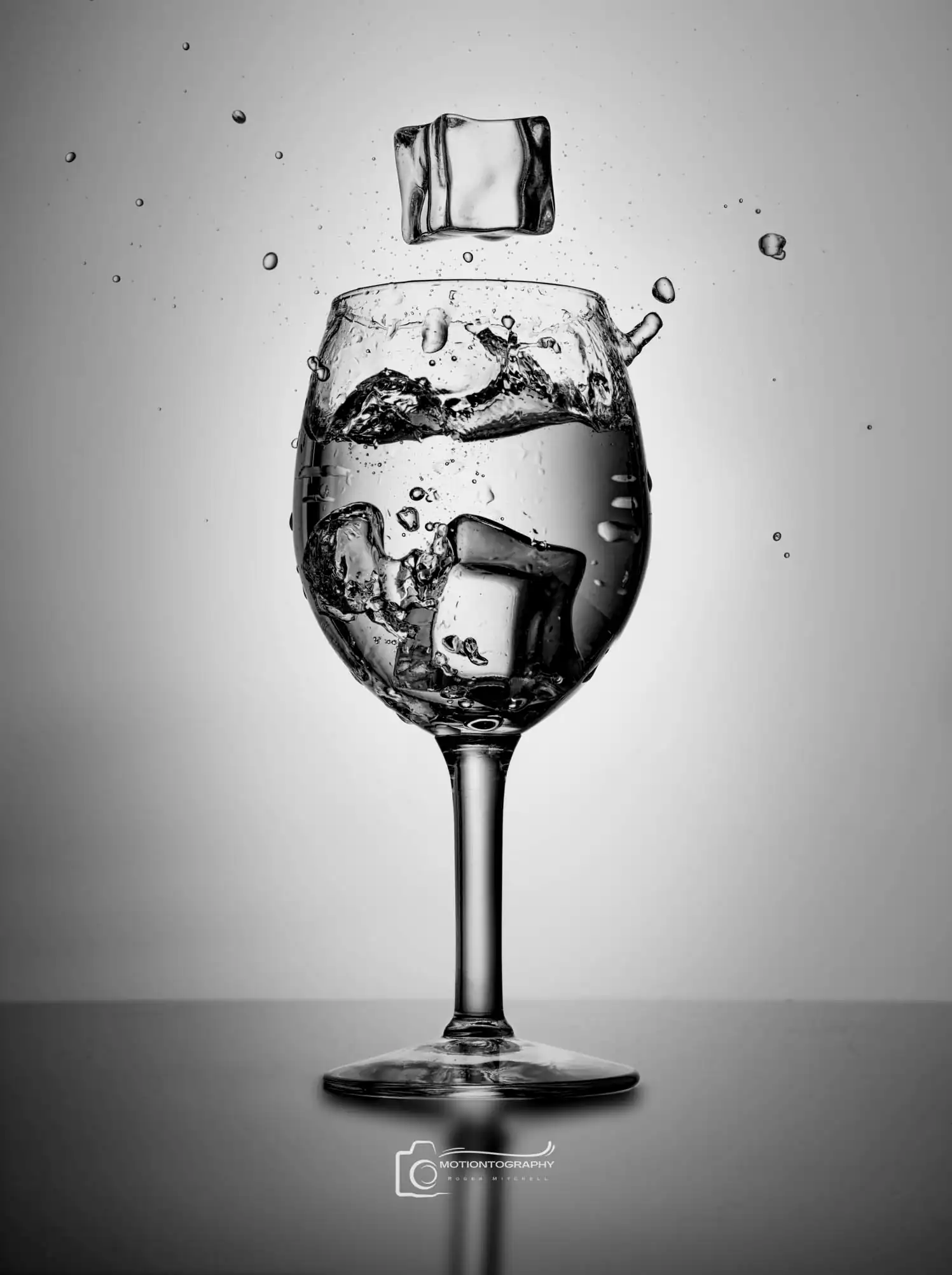 Black and white photo of a wine glass with ice cubes splashing into water, creating a dramatic splash effect